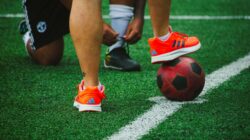 Catatan Sepak Bola: FIFA ASEAN Cup 2026: Perdana Menteri Malaysia Ajak Warga Dukung Harimau Malaya di GBK 2 Close-up pemain sepak bola saat latihan, satu mengikat tali sepatu, yang lain menyeimbangkan bola di rumput.