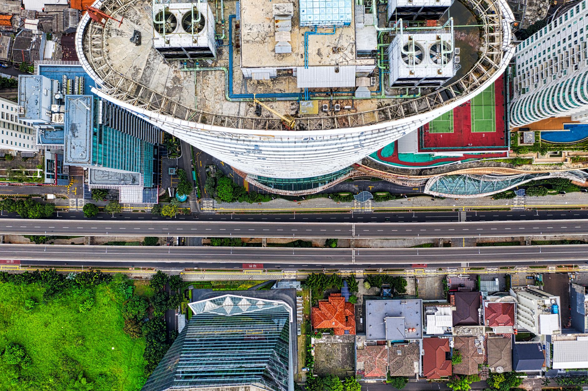 Jepretan drone yang menangkap cakrawala kota Jakarta dengan gedung pencakar langit, jalan, dan area hijau.