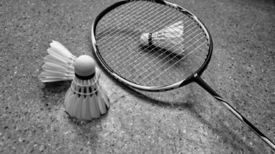Gambar grayscale dari raket badminton dan kok di permukaan lapangan.
