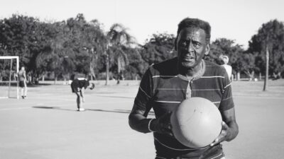Seorang pria tua memegang bola basket di lapangan luar, memancarkan tekad.
