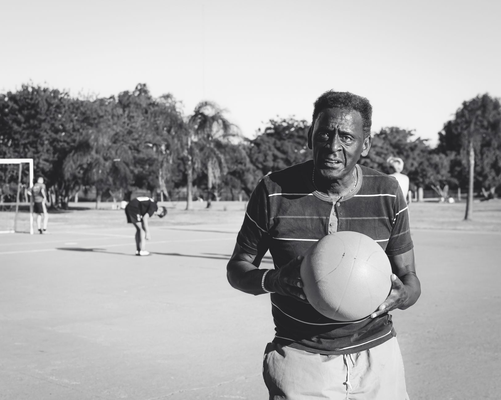 Seorang pria tua memegang bola basket di lapangan luar, memancarkan tekad.