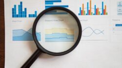 Kaca pembesar memfokuskan pada berbagai grafik dan diagram bisnis di atas kertas.