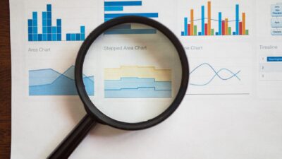 Kaca pembesar memfokuskan pada berbagai grafik dan diagram bisnis di atas kertas.