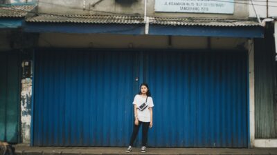 Seorang wanita muda dalam pakaian kasual berdiri di depan penutup logam biru di Indonesia.