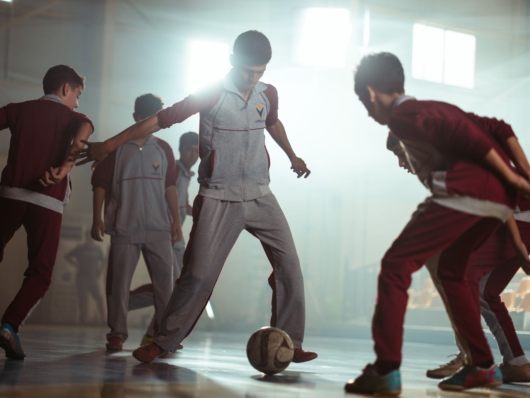 Sekelompok anak laki-laki terlibat dalam permainan sepak bola dalam ruangan yang meriah, menunjukkan kerja sama tim dan energi.