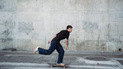 Seorang pria muda yang mahir bermain skateboard di lingkungan perkotaan, mengekspresikan kebebasan dan kelincahan.