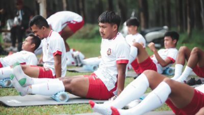 Pemain sepak bola dalam sesi latihan melakukan peregangan di lapangan di Jakarta.