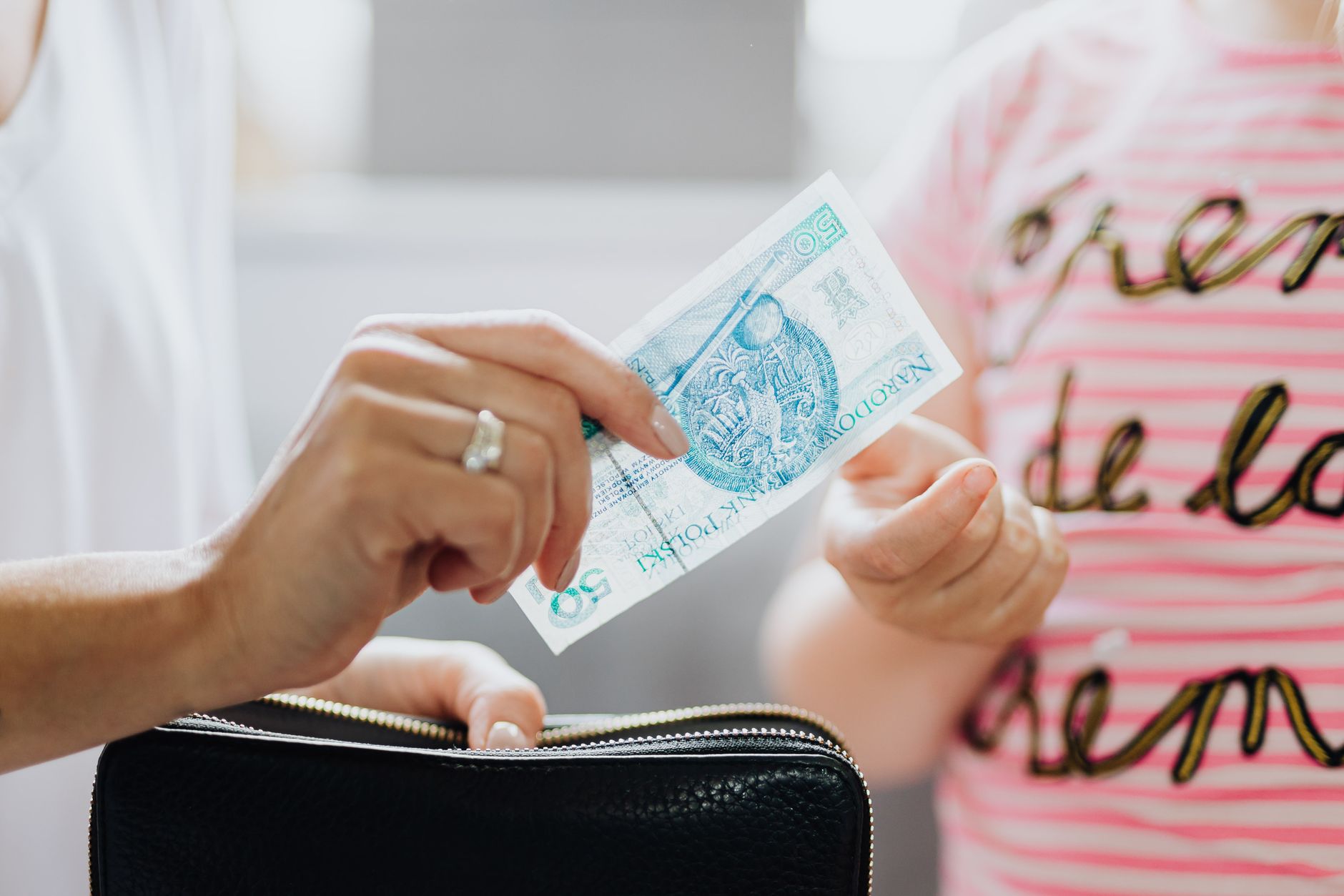 Dekat tangan yang menukarkan uang kertas 50 zloty Polandia, menyoroti transaksi keuangan.