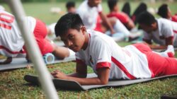 Pemain sepak bola muda yang ikut pelatihan di luar ruangan berbaring di matras latihan.