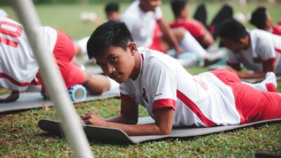 Pemain sepak bola muda yang ikut pelatihan di luar ruangan berbaring di matras latihan.