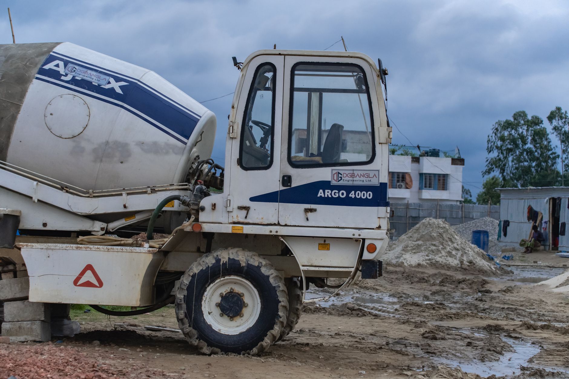 Tampilan dekat truk pengaduk beton di lokasi konstruksi di bawah langit berawan.