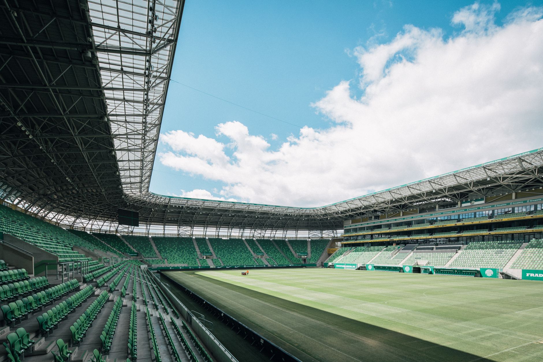 Pemandangan stadion modern di Budapest, Hungaria, dengan kursi hijau dan langit yang luas.