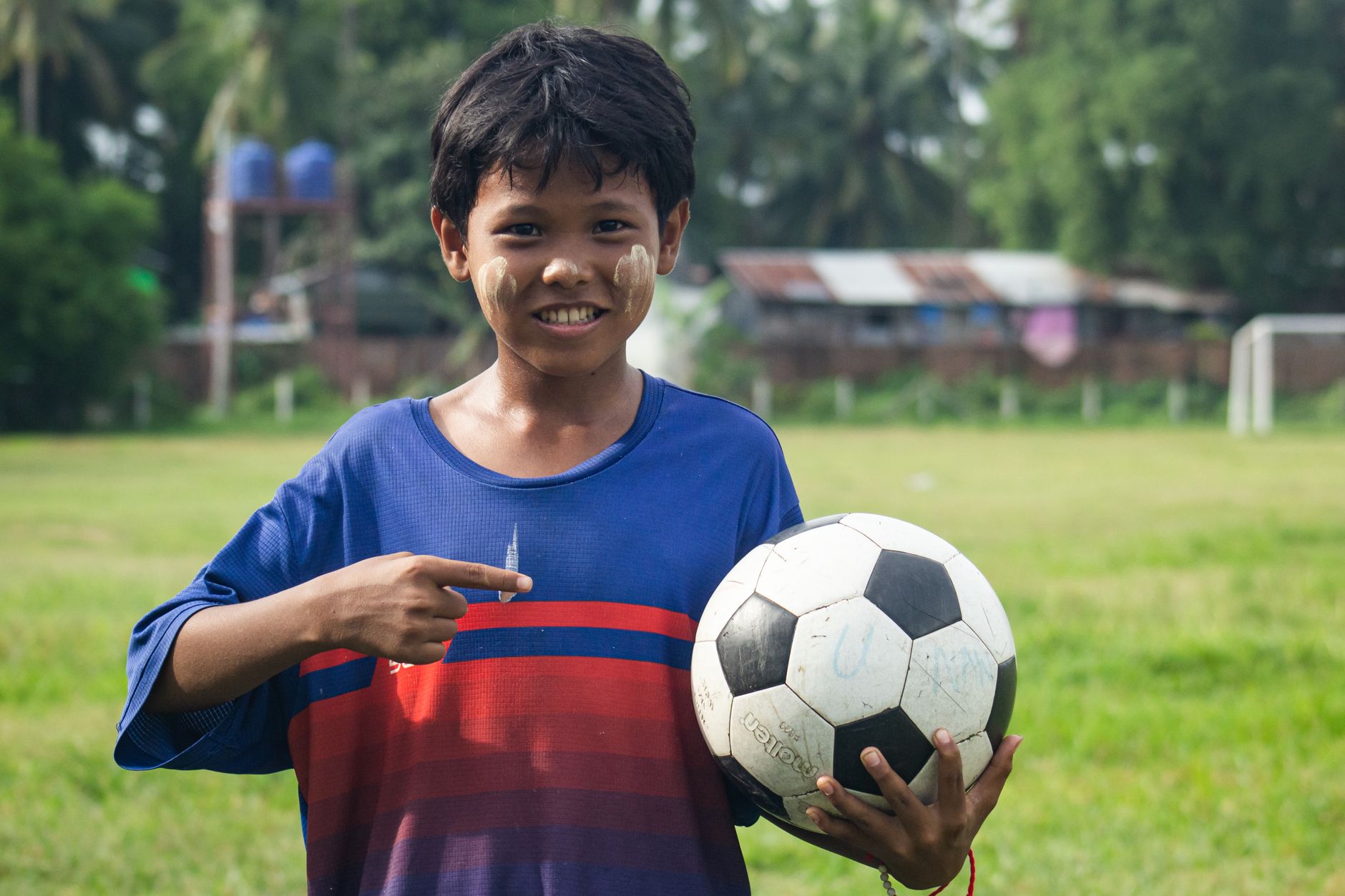 Bocah tersenyum dengan thanaka di wajahnya memegang bola sepak di Myawaddy, Myanmar.