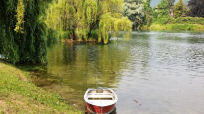 Pemandangan sungai yang tenang dengan perahu dayung merah dan pohon willow di Brivio, Italia.