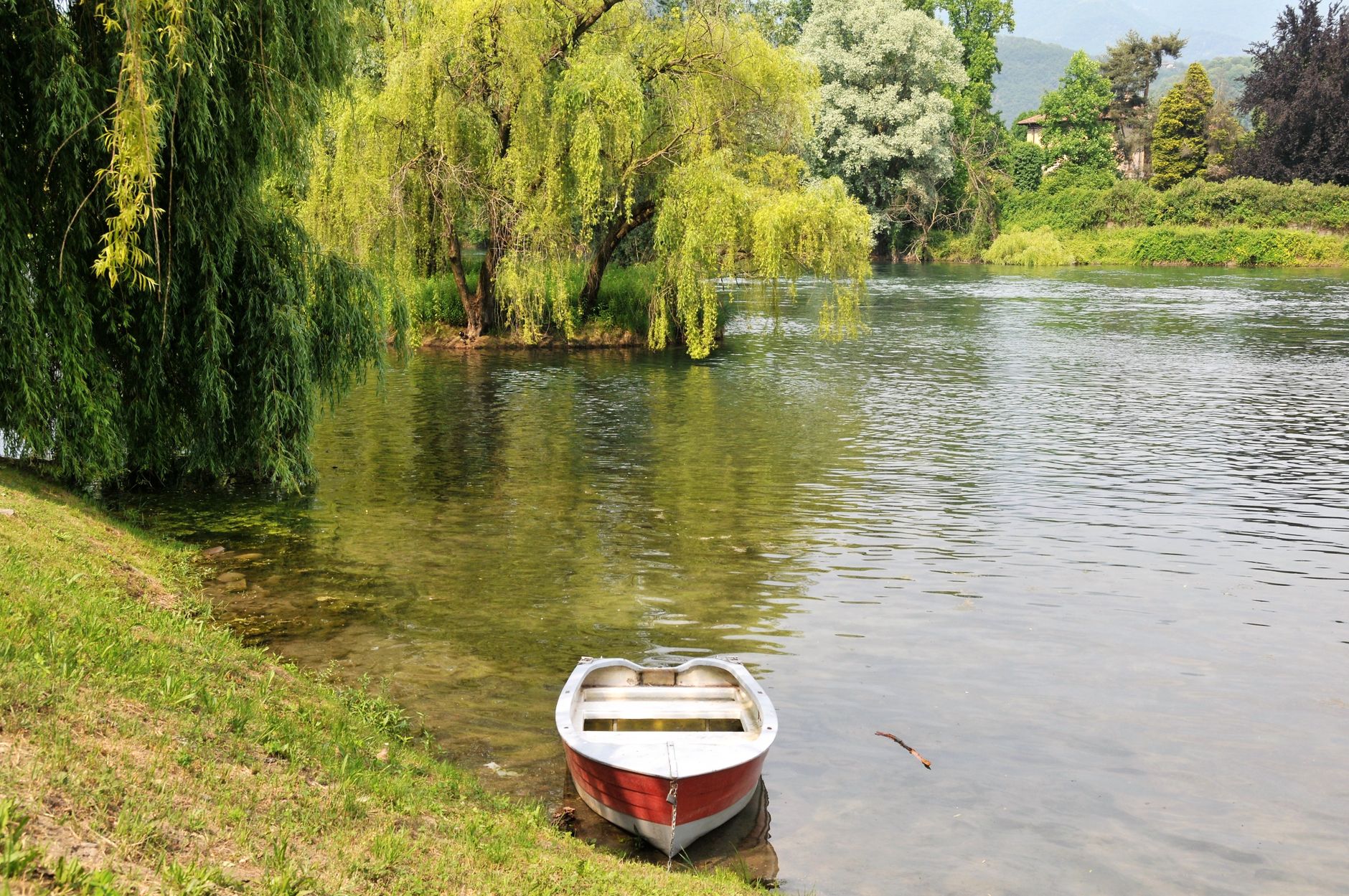Pemandangan sungai yang tenang dengan perahu dayung merah dan pohon willow di Brivio, Italia.