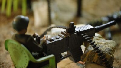 Close-up tentara mainan dalam pengaturan diorama, memegang senapan mesin plastik dan duduk di kursi hijau.