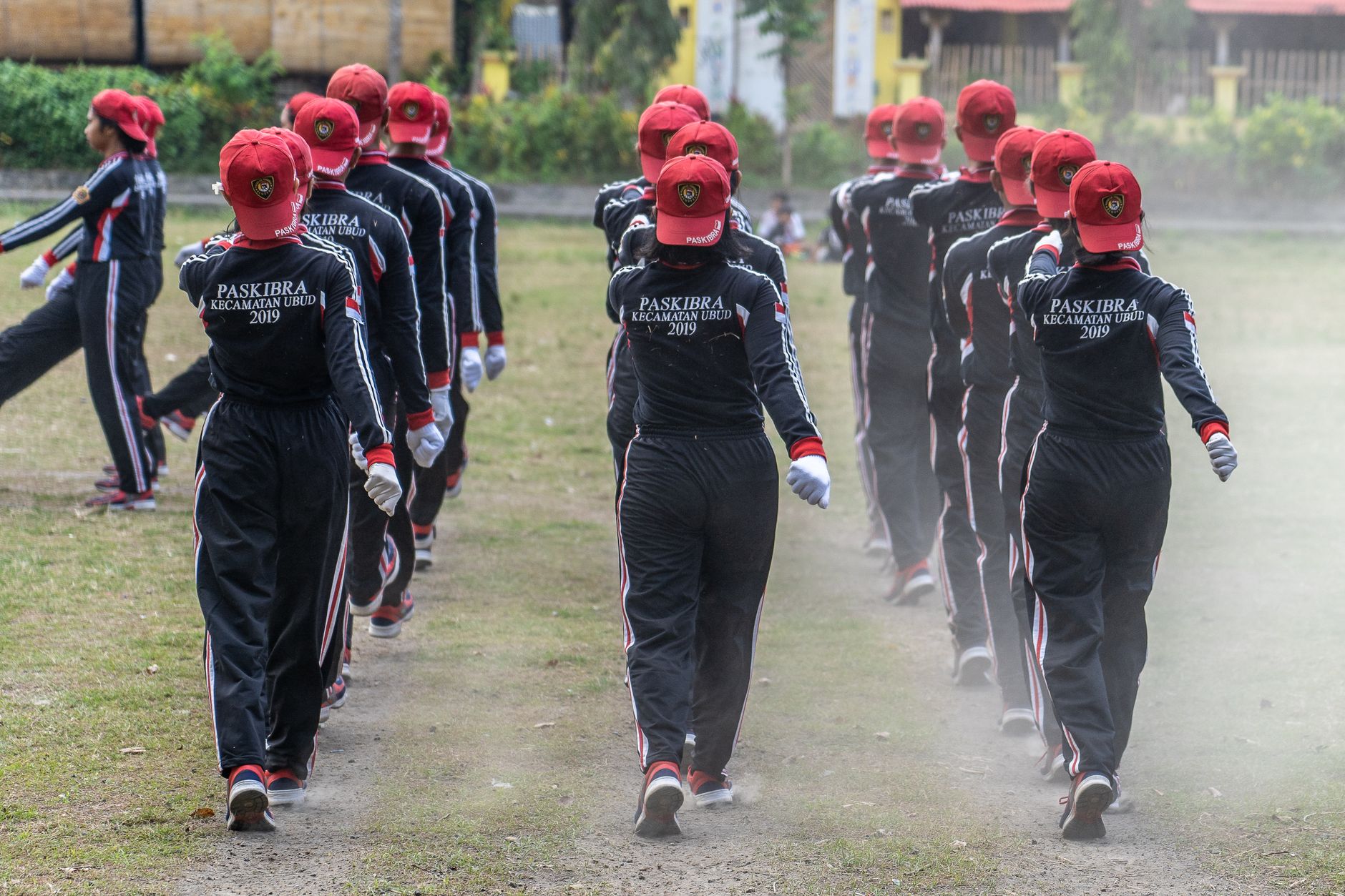 Sekelompok anggota Paskibra yang berbaris dalam formasi di luar ruangan mengenakan seragam dan topi merah.
