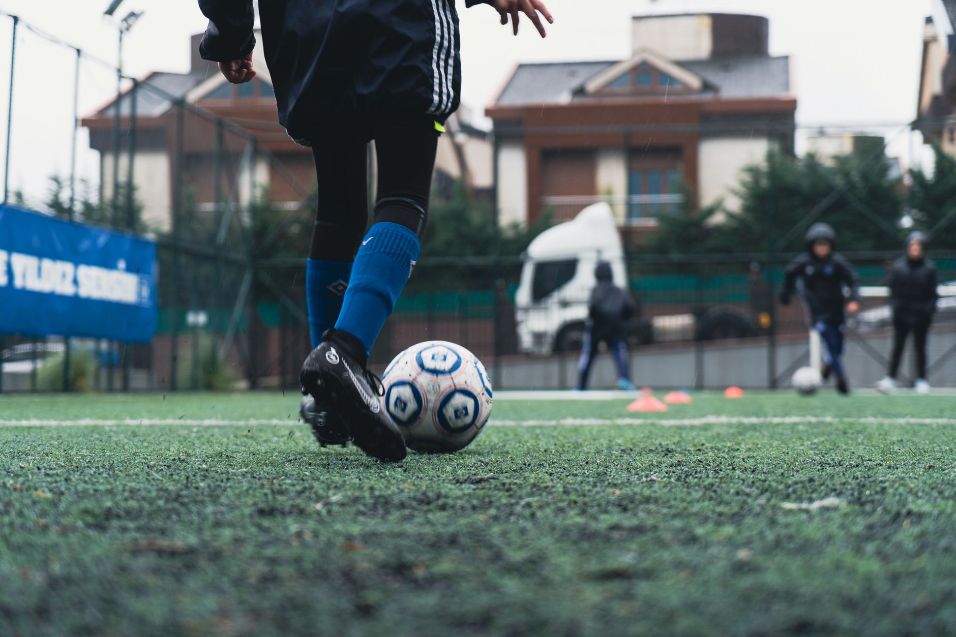 Seorang pemain sepak bola muda dengan kaus kaki biru berlatih di lapangan luar.