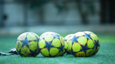 Empat bola sepak yang cerah beristirahat di lapangan rumput hijau.