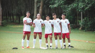 Sekel pemain sepak bola muda berpose dalam seragam tim di lapangan hijau yang subur. Pengaturan olahraga luar ruangan.