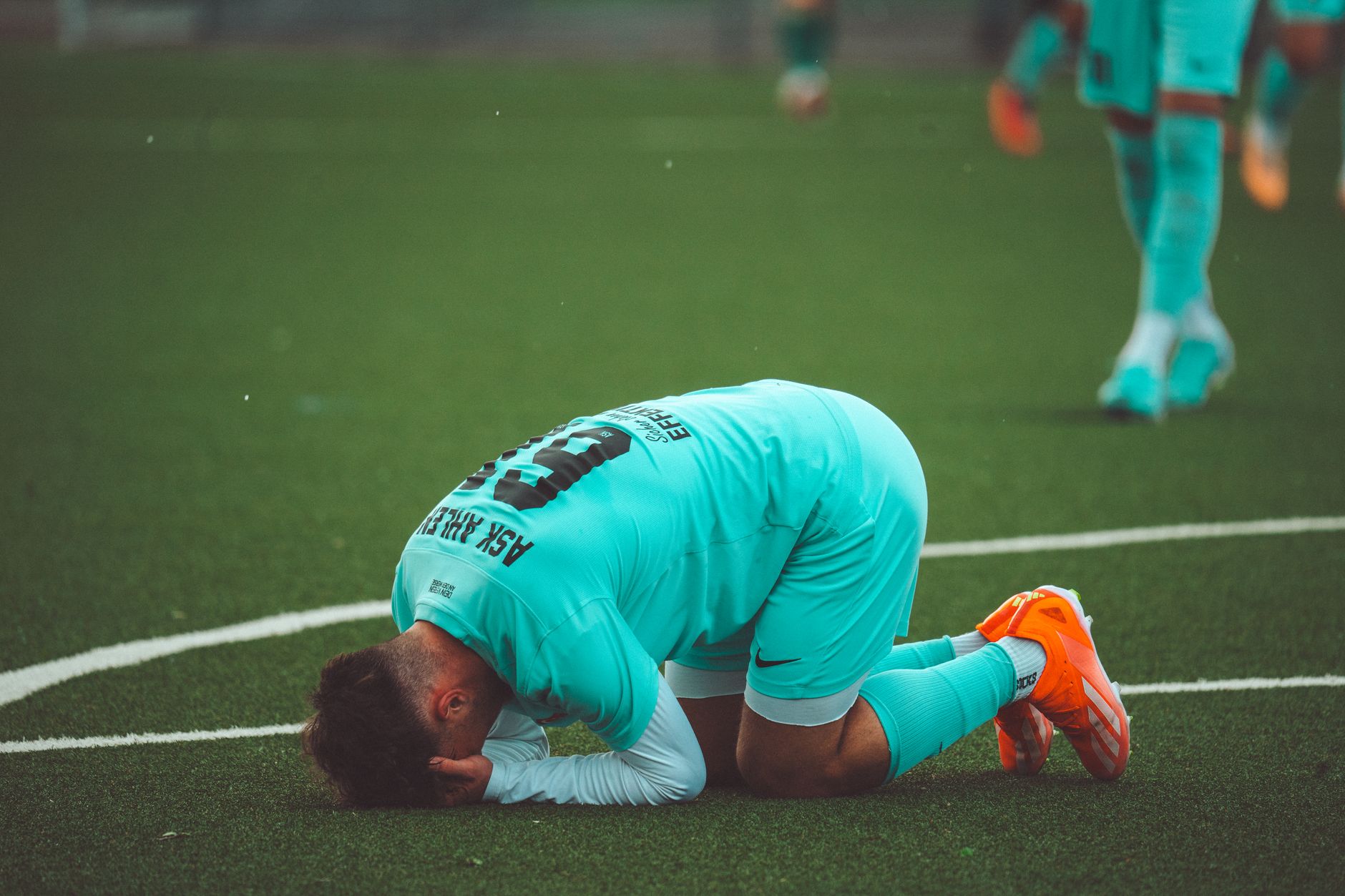 Seorang pemain sepak bola berlutut dalam keputusasaan di lapangan olah raga rumput sintetis hijau.