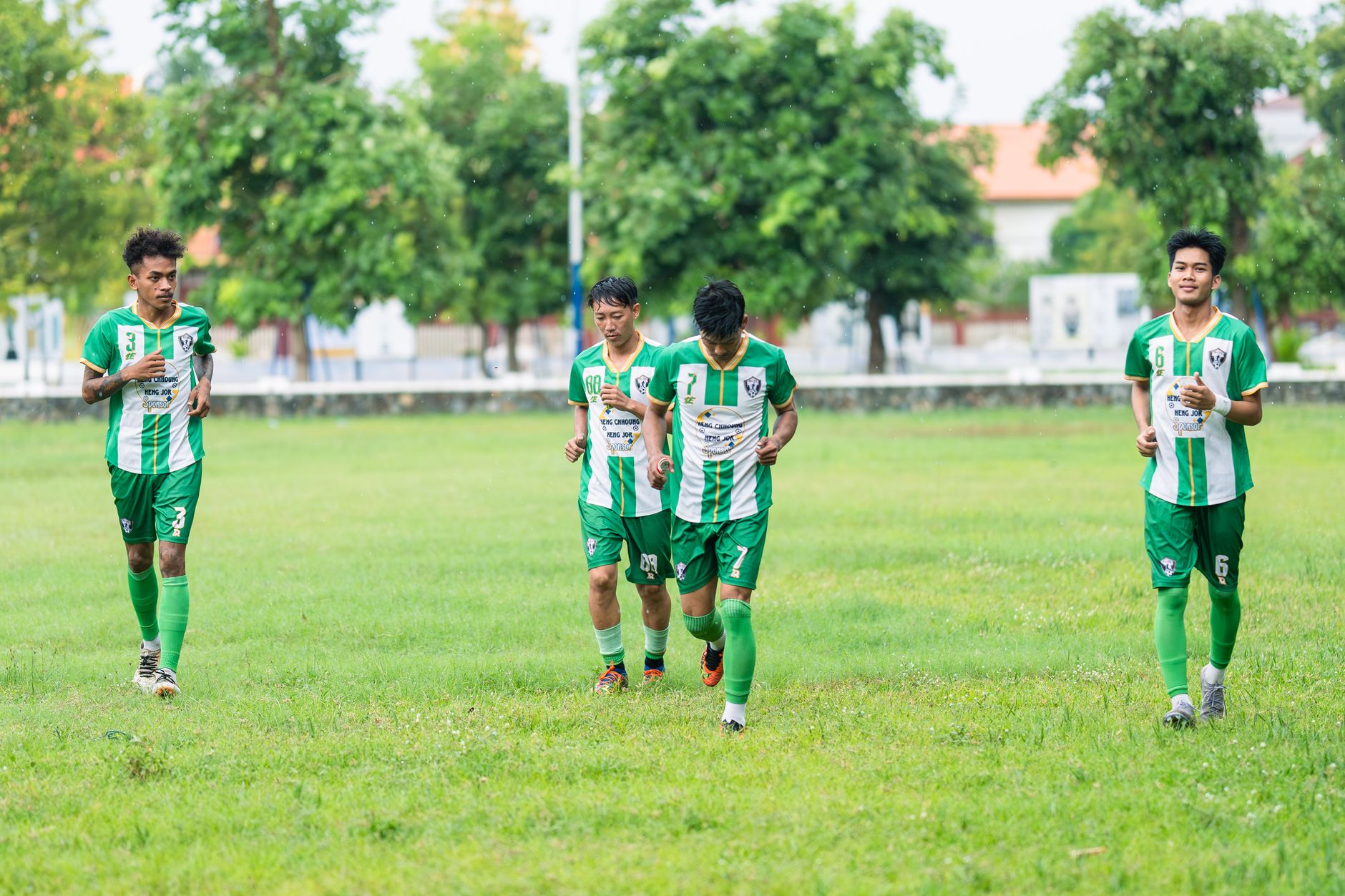 Empat pemain sepak bola muda dengan seragam hijau berlatih di lapangan berumput pada siang hari.