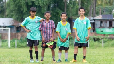 Empat anak laki-laki muda berseragam sepak bola berpose di lapangan rumput di Myawaddy, Myanmar.