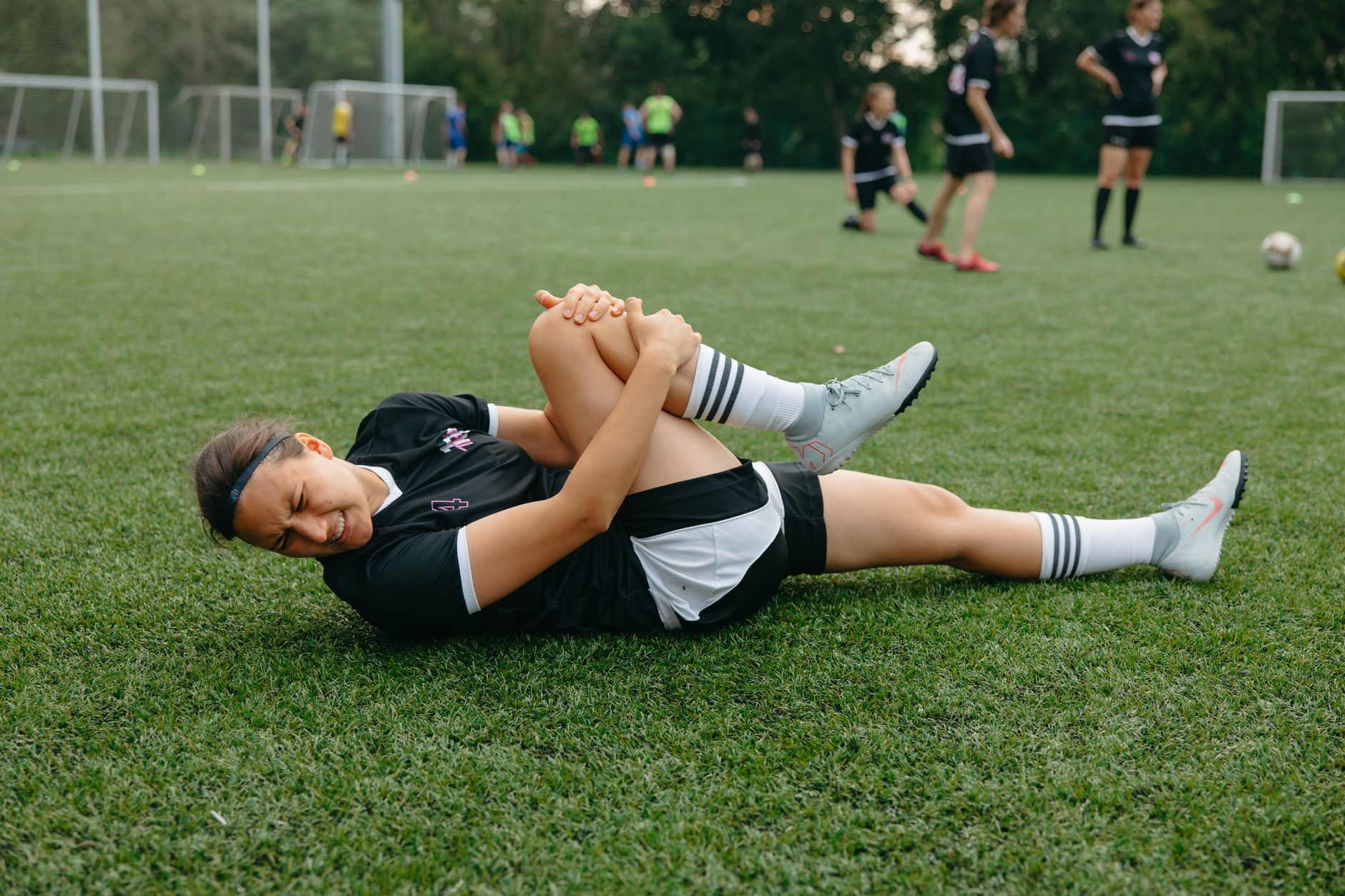 Seorang pemain sepakbola perempuan tergeletak di lapangan, memegang kaki yang terluka dengan rasa sakit selama pertandingan.