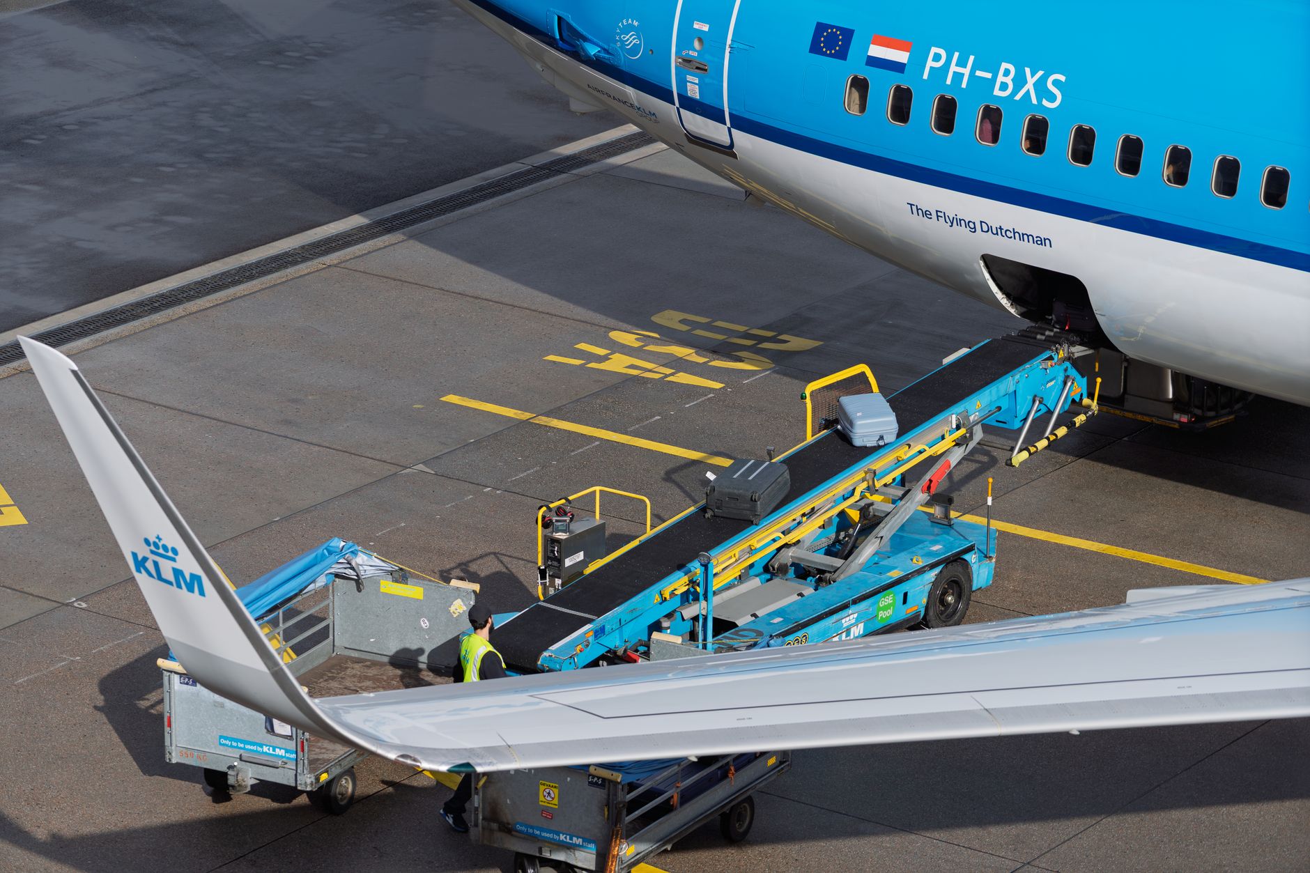Sebuah pesawat KLM sedang dimuati bagasi di bandara, tertangkap kamera di landasan.