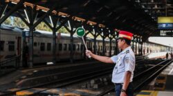 Petugas stasiun kereta api memegang papan sinyal di peron stasiun, siap untuk keberangkatan kereta.