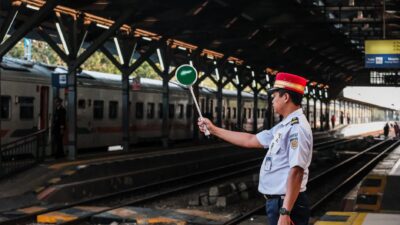 Petugas stasiun kereta api memegang papan sinyal di peron stasiun, siap untuk keberangkatan kereta.