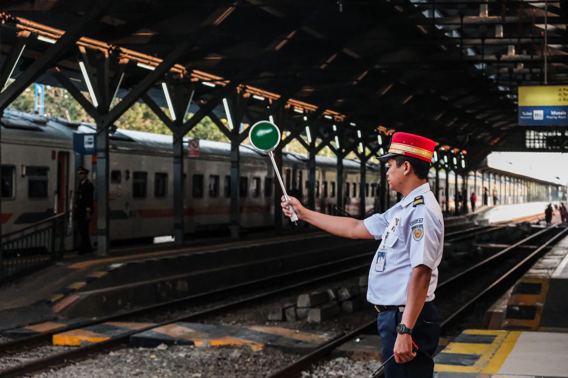 Petugas stasiun kereta api memegang papan sinyal di peron stasiun, siap untuk keberangkatan kereta.