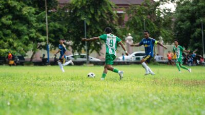 Pertandingan sepak bola dinamis yang dimainkan di lapangan berumput dengan para pemain yang antusias beraksi.