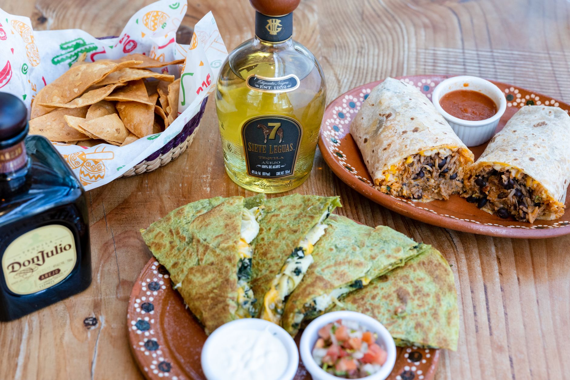 Meja rustic dengan burrito Meksiko, quesadilla, salsa, dan tequila untuk pengalaman bersantap yang otentik.