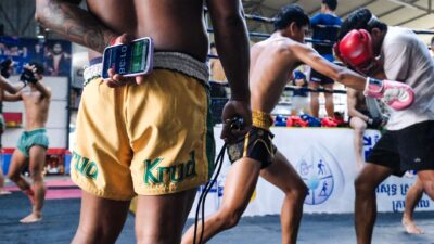 Adegan dinamis para petarung Muay Thai berlatih di sebuah sasana dengan seorang pelatih yang mengatur waktu sesi latihan.