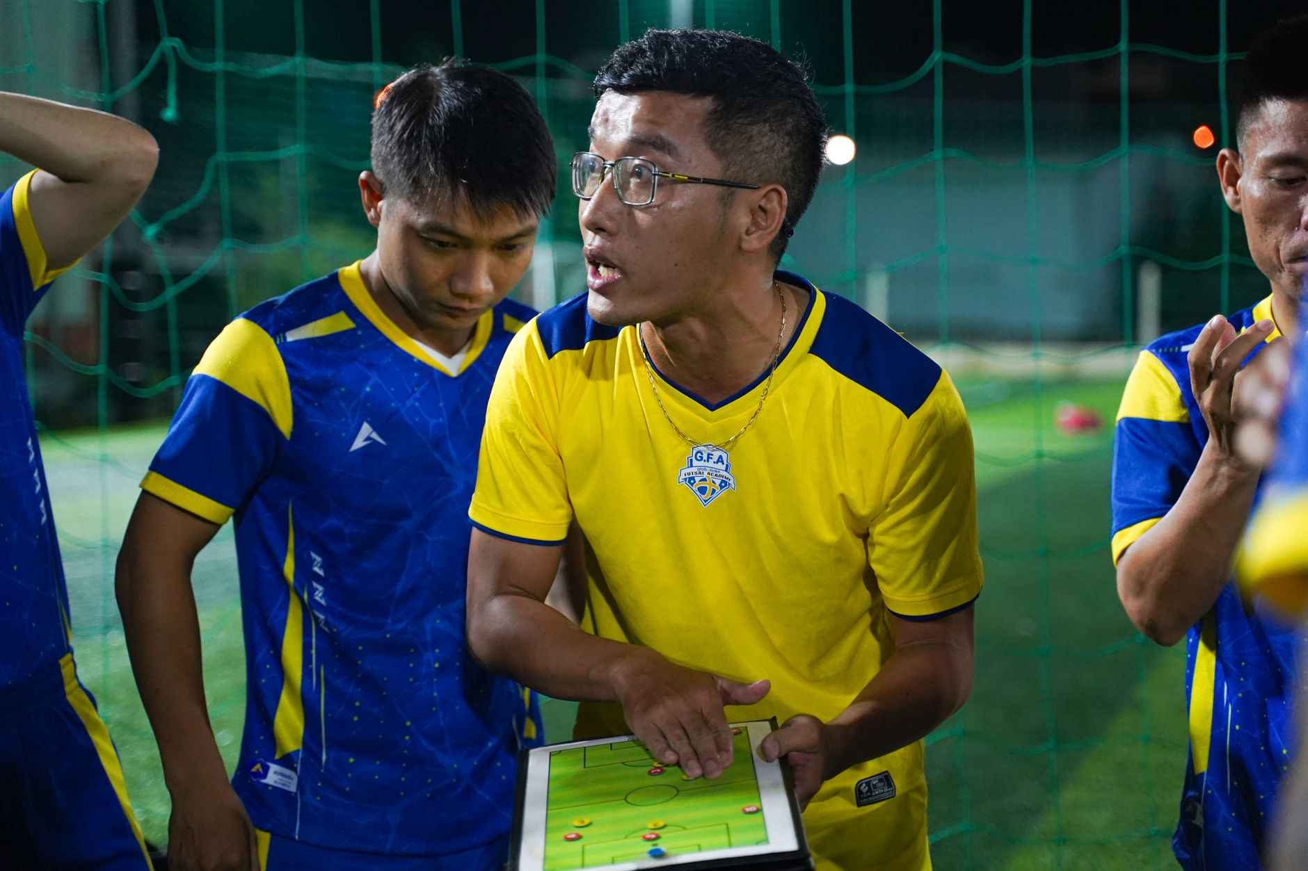 Pelatih mendiskusikan taktik permainan dengan tim sepak bola menggunakan tablet di lapangan.