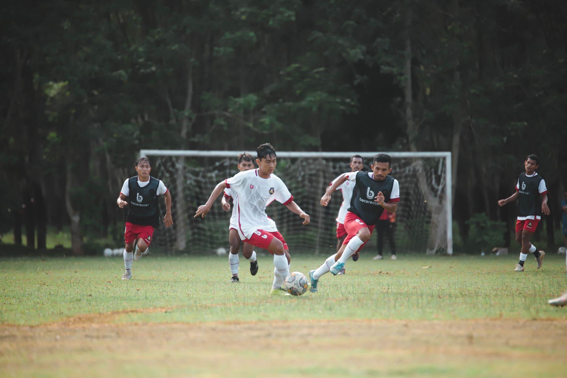 Pengambilan gambar aksi dinamis pemuda bermain sepak bola di lapangan luar yang subur.