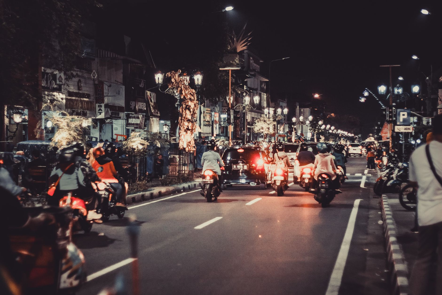 Jalan malam yang meriah dengan mobil dan sepeda motor. Kehidupan perkotaan dan cahaya cerah menangkap esensi energi pusat kota.