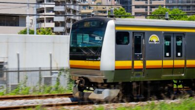 Kereta seri E233 di Jalur Nambu melintas di perkotaan Tokyo pada siang hari.