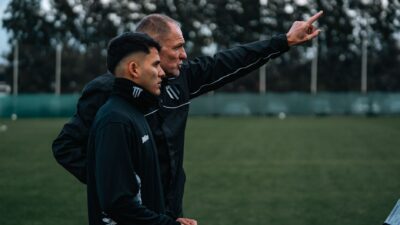 Sorotan: Luciano Leandro Soroti Taktik Pelatih Timnas Indonesia di 3 Laga FIFA ASEAN Cup 2026: Agre... 8 Seorang pelatih sepak bola berdiskusi tentang strategi dengan seorang pemain muda selama latihan di luar ruangan.