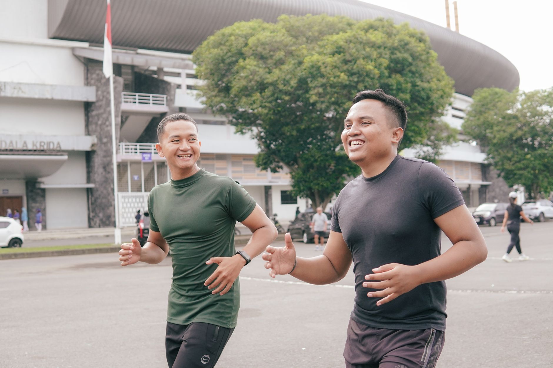 Dua pria ceria sedang jogging di dekat stadion, mempromosikan kebugaran dan persahabatan.