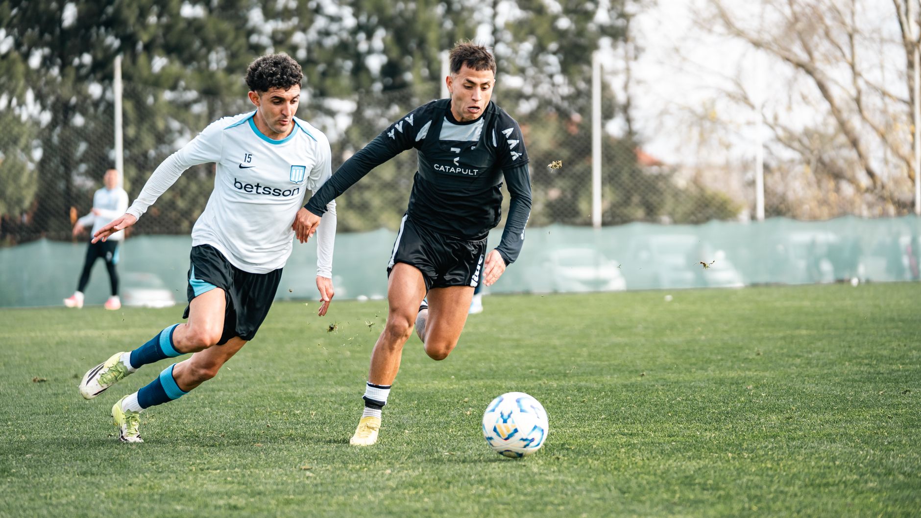 Foto aksi dinamis dua pemain sepak bola yang bersaing dengan intens di lapangan saat siang hari.