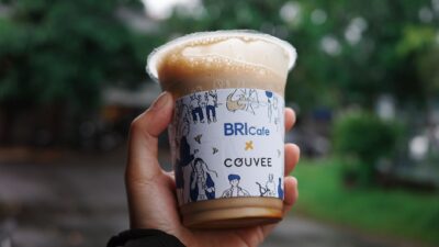 Update: BRI Super League: Igor Tolic Yakin Garudayaksa Tampil All Out, Persib Harus Waspada 8 Close-up tangan memegang cangkir kopi es bermerek di luar ruangan, dengan latar belakang hijau buram yang cerah.