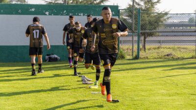 Tim sepak bola melakukan pemanasan di lapangan, mengenakan seragam olahraga.