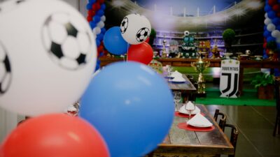 Pengaturan pesta sepak bola yang berwarna-warni di dalam ruangan dengan balon dan set meja, sempurna untuk para penggemar olahraga.