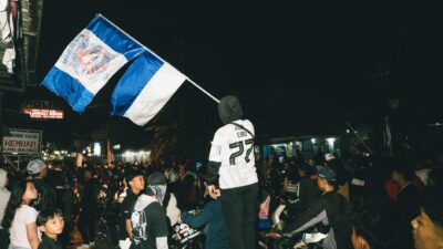 Update: Pelaku Pembunuhan Bobotoh Persib Ditangkap, Umuh Muchtar Apresiasi Polresta Bogor 3 Sebuah kumpulan jalanan yang meriah di malam hari dengan bendera yang ditampilkan secara mencolok di tengah kerumunan besar.
