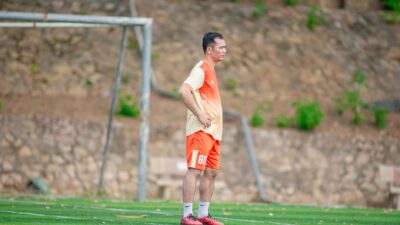 Seorang pria mengenakan pakaian olahraga berdiri di lapangan sepak bola pada siang hari.